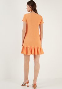 Short-sleeve orange dress with a textured fabric, fitted bodice, and flared ruffle hem. The back features a simple, clean neckline.
