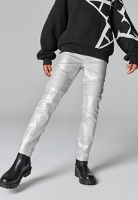 Silverfärgade fusk läderbyxor med ribbade detaljer, slim fit och sömnadsdetaljer. Kombineras med en svart sweatshirts och kraftiga svarta stövlar.
