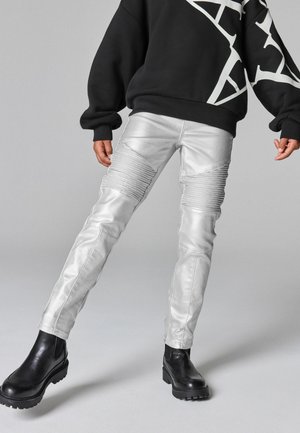 Pantaloni in pelle sintetica argentata con accenti a coste, vestibilità slim e dettagli di cucitura. Abbinati a un maglione nero e stivali neri robusti.