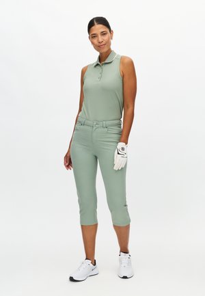 Polo verde chiaro senza maniche con colletto, abbinata a pantaloni capri verde chiaro. Guanto da golf bianco sulla mano sinistra, scarpe bianche con dettagli neri.