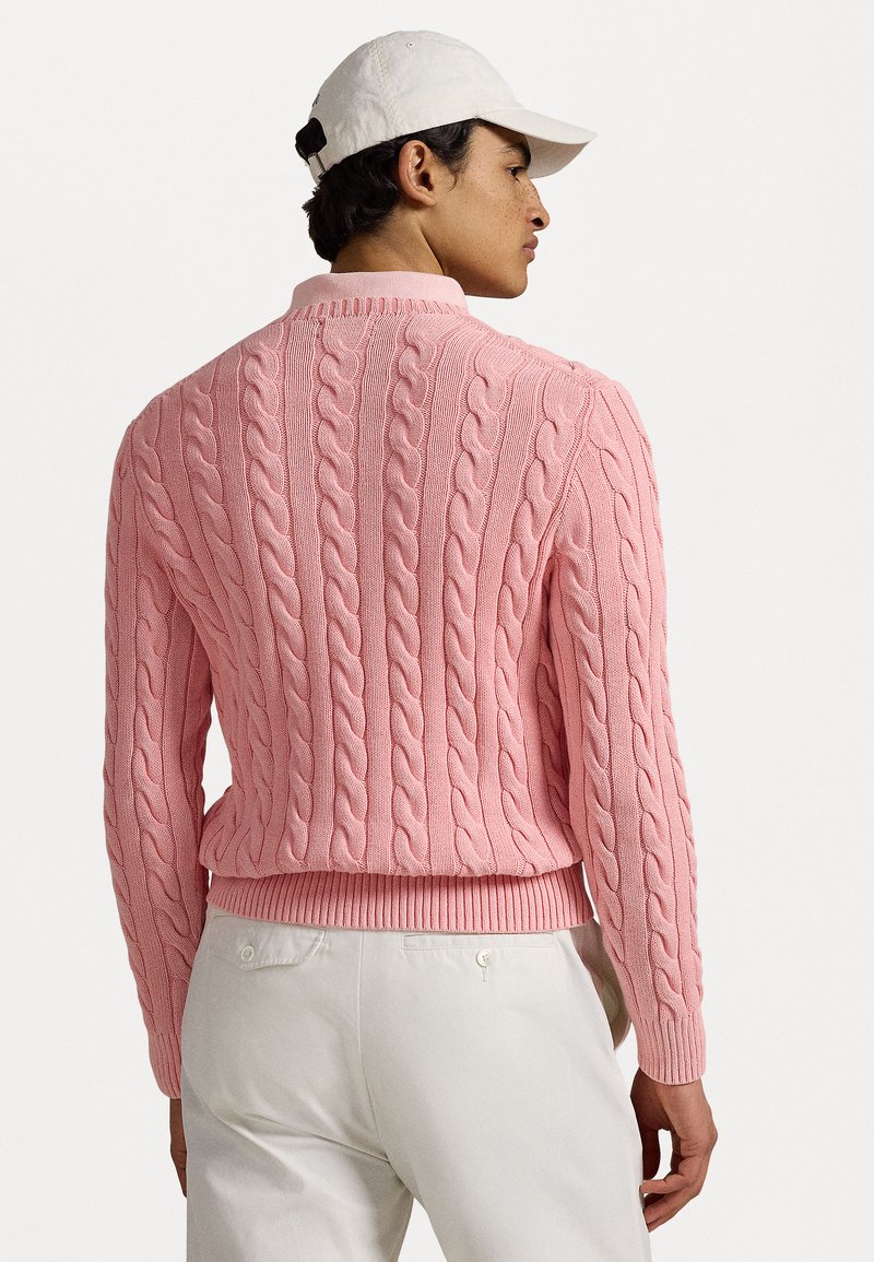 Sweter w warkoczowym splocie w pastelowym różu z dopasowanym dołem. Teksturowany wzór z tyłu, długie rękawy i okrągły kołnierzyk. W połączeniu z jasnymi spodniami.