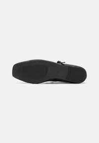 Schwarze Schuhsohle mit einer strukturierten GummOberfläche, die Rillen, gebogene Kanten und ein glattes Finish aufweist. Ein kleines dekoratives Element ist vorhanden.