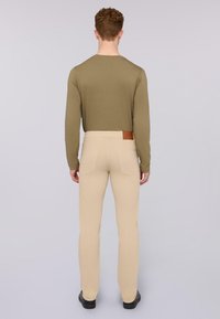 Pantalones ajustados beige con bolsillos traseros, combinados con una camisa de manga larga verde oliva. El tejido parece suave y ligero.