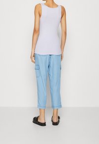 Light purple tank top paired with light blue cargo pants, featuring side pockets and a cropped length. Black slip-on shoes.