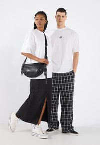 Fehér oversized pólók, fekete farmer maxi szoknya oldalsó hasítékkal, fekete bőrtáska keresztpánttal, kockás nadrágok és fehér sportcipők.