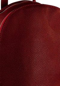 Sac à dos en cuir texturé rouge avec un haut incurvé et une fermeture éclair en argent visible le long du bord.