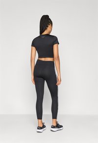 Μαύρο κοντομάνικο μπλουζάκι και ψηλόμεσα κολάν με λεπτομέρεια λογότυπου στο πλάι. Ύφασμα από ζέρσεϊ, στενή εφαρμογή, συνδυασμένο με μαύρα αθλητικά παπούτσια.