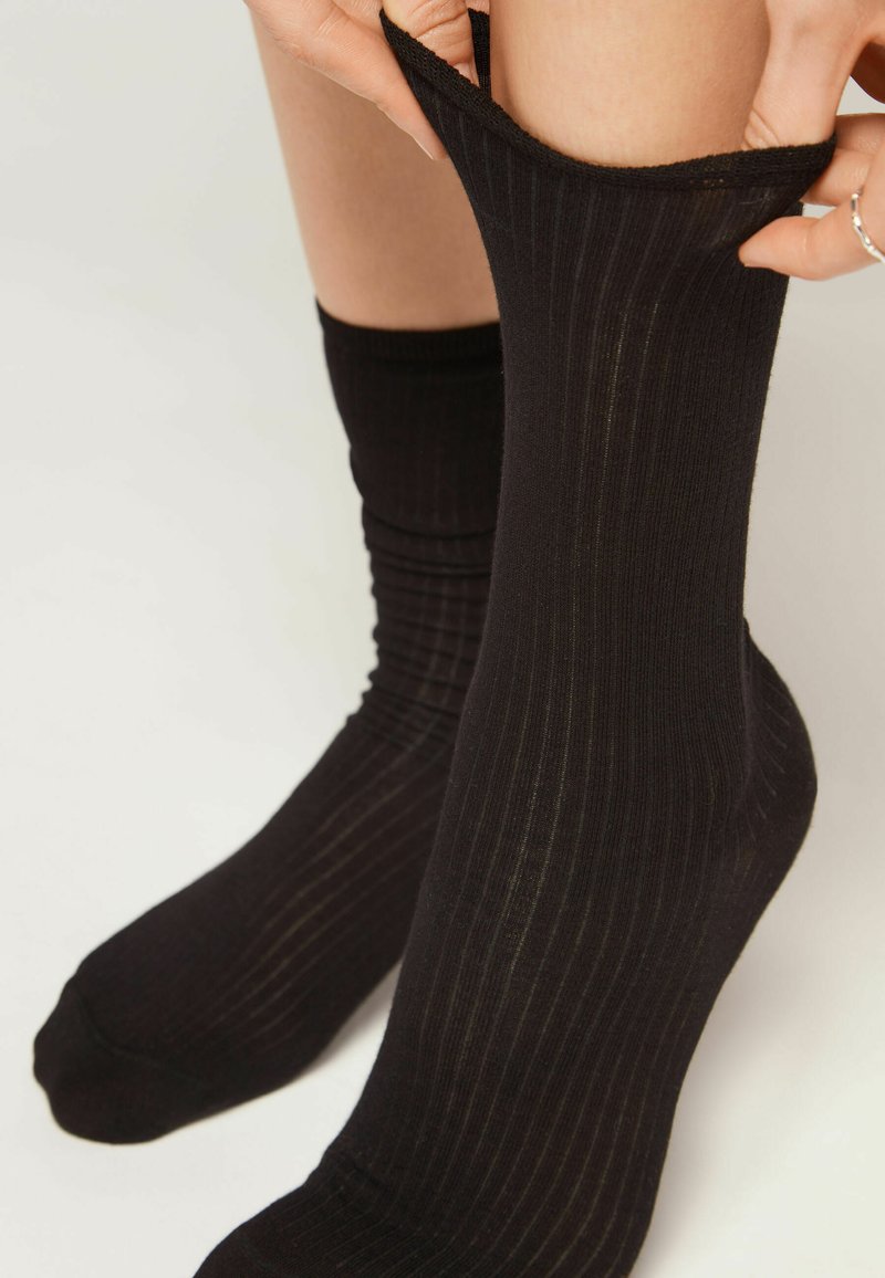Calcetines negros de canalé con un diseño texturizado, que llegan hasta la mitad de la pantorrilla. La tela parece elástica y ajustada alrededor de la pierna.