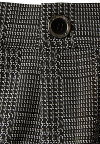 Tessuto a righe bianche e nere con un primo piano di un elastico che presenta un bottone nero, mostrando un design texture e strutturato.