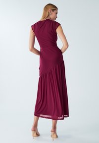 Bordo spalvos maxi suknelė iš minkštos medžiagos, su prigludusiu bodžetu ir surinktu sijonu. Trumpomis rankovėmis ir lengvu siluetu.
