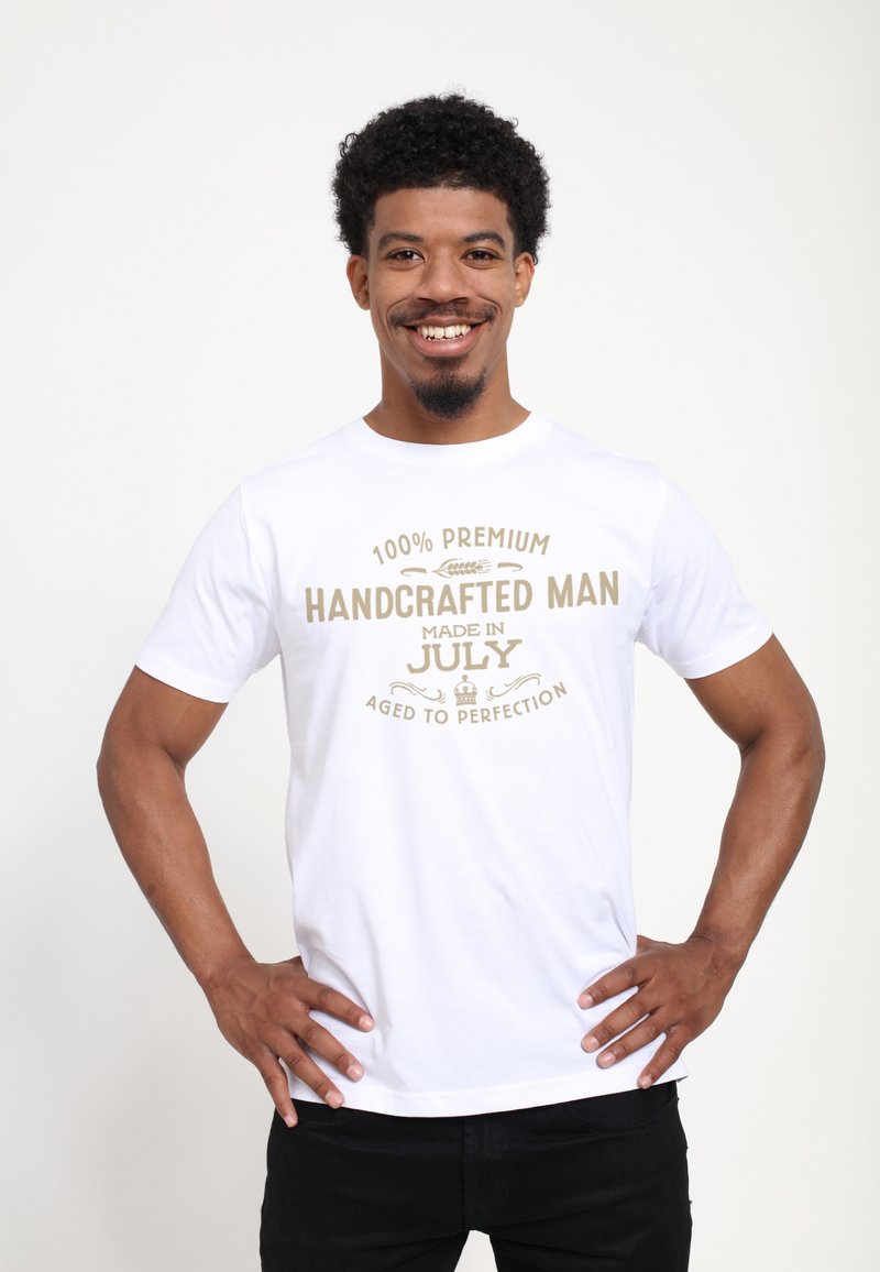 Camiseta de algodón blanca con texto dorado: "100% Premium Hecho a Mano, Fabricado en Julio, Madurado a la Perfección." Cuello redondo, mangas cortas.