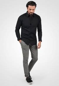 Svart langermet skjorte med knapper, grå slim-fit bukser og svarte joggesko. Skjorten har en brystlomme og en skreddersydd passform.