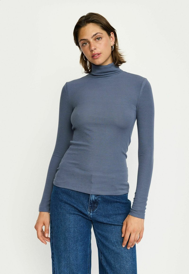 Maglione grigio a collo alto con maniche lunghe, slim fit, realizzato in un morbido tessuto, abbinato a jeans in denim blu a vita alta.