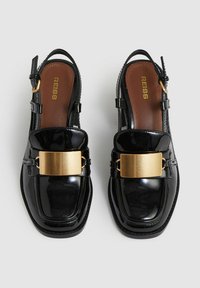 Čierne lakované kožené slingback topánky so štvorcovou špičkou, zlatým kovovým detailom a hnedou stielkou. Majú nastaviteľný popruh na členku.