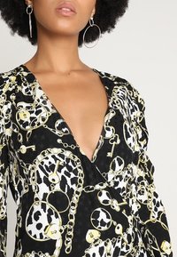 Robe en imprimé léopard noir et blanc avec motif de chaîne en or et de clé. Design à encolure en V, manches longues, tissu lisse avec accents audacieux.