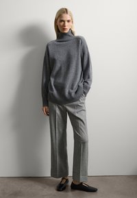 Suéter de punto gris con cuello alto y borde acanalado, combinado con pantalones de lana gris de pierna ancha que presentan una sutil textura y dobladillos rematados. Zapatos planos negros.