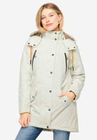 Vaaleanharmaa, vedenpitävä parka, jossa on korkea kaulus, kiinnitetty huppu ja vetoketjulliset taskut oransseilla yksityiskohdilla. Teksturoitu kangas ja rento istuvuus.