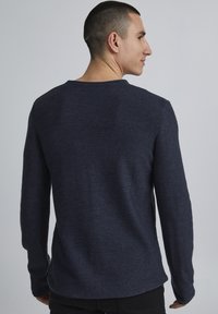 Dunkelblaues langärmliges Sweatshirt mit strukturiertem Strickmuster, runder Ausschnitt und enganliegenden Bündchen, von hinten gezeigt.