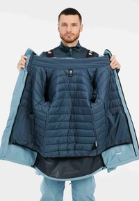 Gevoerde jas met een marineblauw interieur, ritssluitingen en een lichtblauwe buitenkant. Het interieur bevat netvakken en een labeldetail.