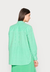Camisa riscada verde e branca com uma pala às costas, mangas longas, punhos abotoados e um corte relaxado. Tecido suave com uma textura nítida.