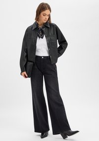 Czarna kurtka z eko skóry, szerokie ciemne jeansy, biała koszula i wzorzysty szalik. Do stroju dołączona jest mała czarna kopertówka i botki na obcasie.