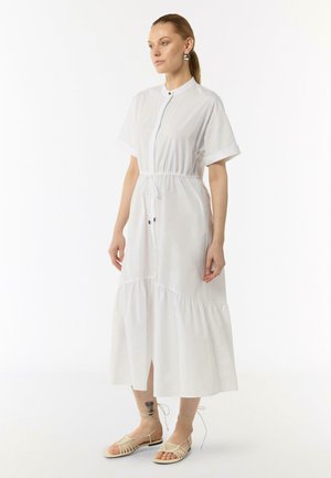 Witte midi-jurk met een knoopsluiting aan de voorkant, korte opgerolde mouwen en een elastische taille. Heeft een gelaagde rok en een zijsplit. Gedragen met sandalen met bandjes.