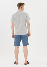 Grå kortärmad t-shirt och blå uppvikta shorts, tillverkade av ett tyg med en jämn textur. Avslappnade skor fulländar outfiten.