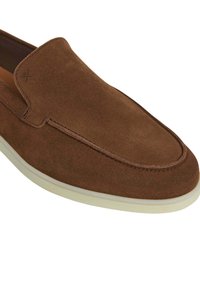 Scarpa slip-on in suede marrone con punta arrotondata, dettagli di cucitura discreti e suola in gomma bianca. Texture liscia e design minimalista.