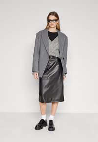 Gray wool blazer over a gray knitted vest, black faux leather skirt, and black platform shoes with white socks. Slim-fit, modern design.