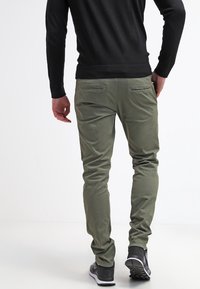 Olivově zelené volné kalhoty s úzkým střihem, vyrobené z měkké textilie. Mají dva zadní kapsy s jemnými švy a zúžené nohavice.