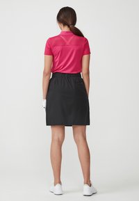 Rosa polo skjorta med randig textur vid axlarna, i kombination med en svart kjol med elastisk midja. Bärs med vita golfsandaler.