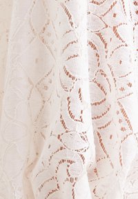 Tissu en dentelle blanche avec des motifs floraux et géométriques comprenant des diamants et des formes semblables à des feuilles sur un textile semi-transparent.