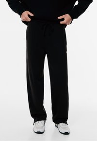 Zwarte sweatpants gemaakt van zachte, gladde stof. Kenmerkt zich door een elastische tailleband met koord en zijzakken. Eenvoudig ontwerp met een logo-accent.