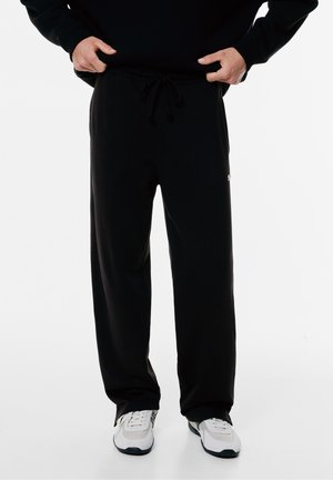 Black sweatpants made of soft, smooth fabric. Features an elastic waistband with drawstring and side pockets. Simple design with a logo accent.