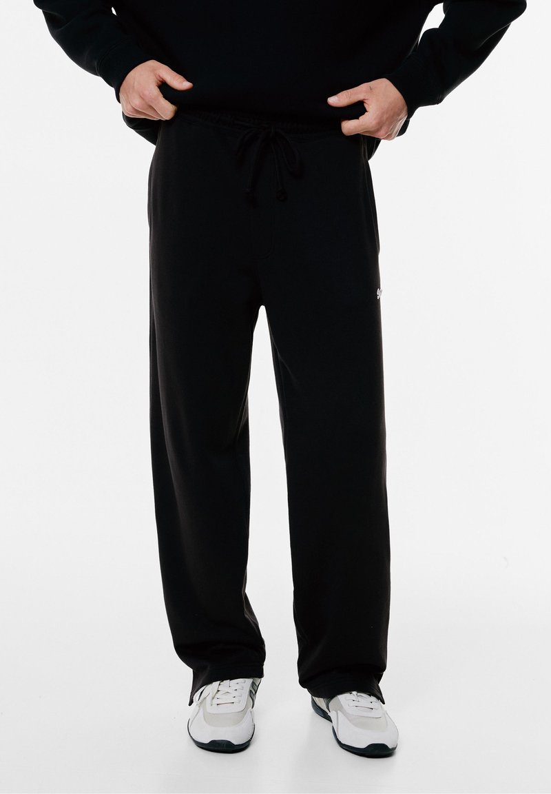 Zwarte sweatpants gemaakt van zachte, gladde stof. Kenmerkt zich door een elastische tailleband met koord en zijzakken. Eenvoudig ontwerp met een logo-accent.