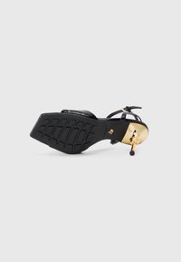 Sandalia negra de tacón con suela de goma texturizada y acento dorado en el tacón. Presenta tiras delgadas para un ajuste seguro y un diseño elegante.