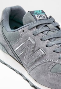 Baskets New Balance 996 grises avec dessus en suède et mesh, logo bleu, col rembourré, lacets et semelle intermédiaire blanche avec semelle extérieure texturée.