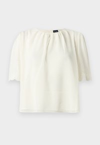 Blouse blanche à manches courtes avec encolure froncée et bords de manches brodés et festonnés, présentée sur un fond uni.