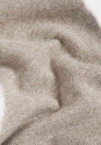 Tejido de lana beige con una superficie suave y texturizada, que presenta un aspecto natural, ligeramente borroso y pliegues suaves.