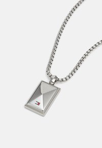 Pendente argento rettangolare con superficie testurizzata, attaccato a una catena d'argento. Presenta un piccolo logo in rosso, bianco e blu alla base.