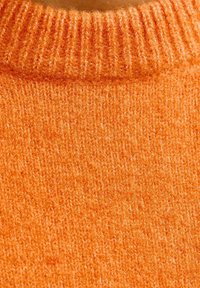 Gros plan sur un tissu tricoté orange, doux et duveteux, avec un bord replié à côtes en haut.