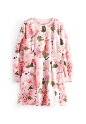 Niño con vestido rosa de flores con mangas abullonadas y zapatillas blancas, de pie frente a un fondo claro y liso.