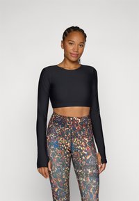 Svart langermet crop topp sammen med fargerike, mønstrede høyt i livet leggings i en blanding av blå, oransje og grønne nyanser.