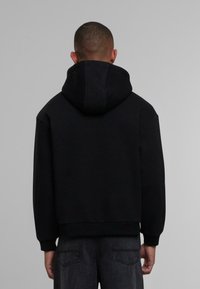 Sudadera negra con una textura suave, capucha con cordón y puños acanalados, combinada con jeans de mezclilla gris oscuro, mostrada desde la parte posterior.