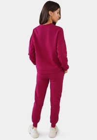 Fuchsia Sweatshirt- und Jogger-Set aus weichem Material, mit lockerer Passform und gerippten Bündchen, kombiniert mit weißen Sneakers.