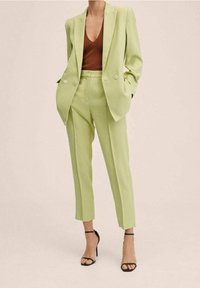 Costume ajusté vert clair avec un blazer structuré et un pantalon fuselé assorti. Le blazer présente des boutons doubles et des poches latérales.