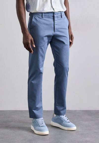 Pantaloni blu chiaro in misto cotone con vestibilità slim, con chiusura a zip classica e tasche laterali. Indossati con sneakers blu chiaro a basso profilo.
