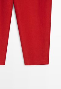 Červené kalhoty s rovnými nohavicemi zobrazené na bílém pozadí, ukazující spodní polovinu a texturu látky.