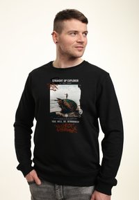 Černá mikina s předním potiskem obsahujícím barevný design skateboardu a text. Materiál vypadá měkce; manžety a lem jsou žebrované.