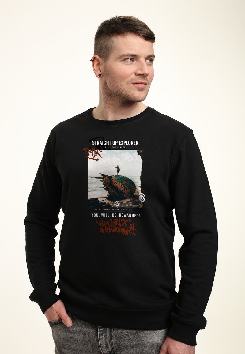 Černá mikina s předním potiskem obsahujícím barevný design skateboardu a text. Materiál vypadá měkce; manžety a lem jsou žebrované.